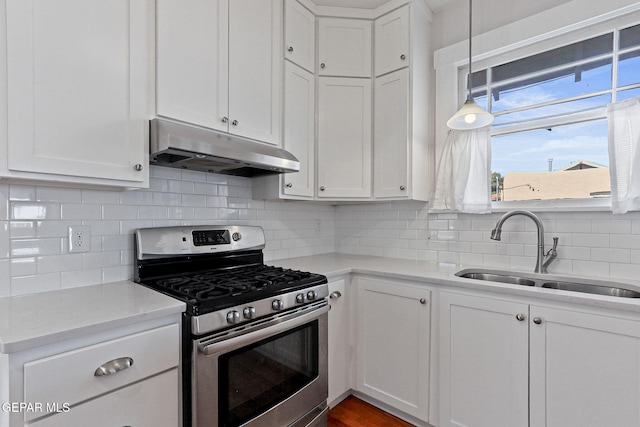 kitchen featuring under cabinet range hood, stainless steel gas range, a sink, white cabinetry, and light countertops