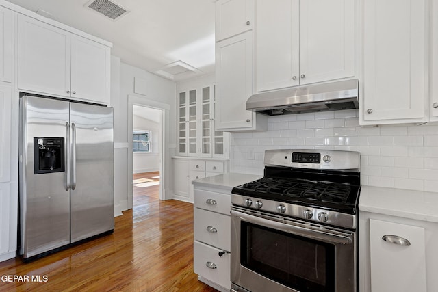 kitchen with stainless steel appliances, under cabinet range hood, light countertops, light wood-style flooring, and white cabinetry