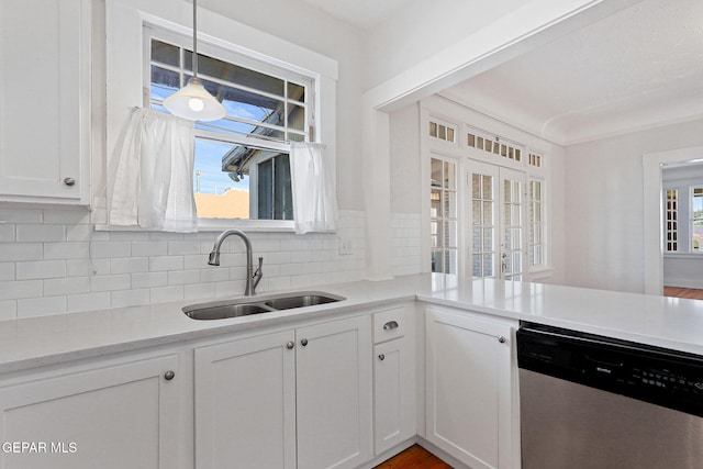 kitchen with stainless steel dishwasher, a sink, decorative backsplash, white cabinets, and hanging light fixtures