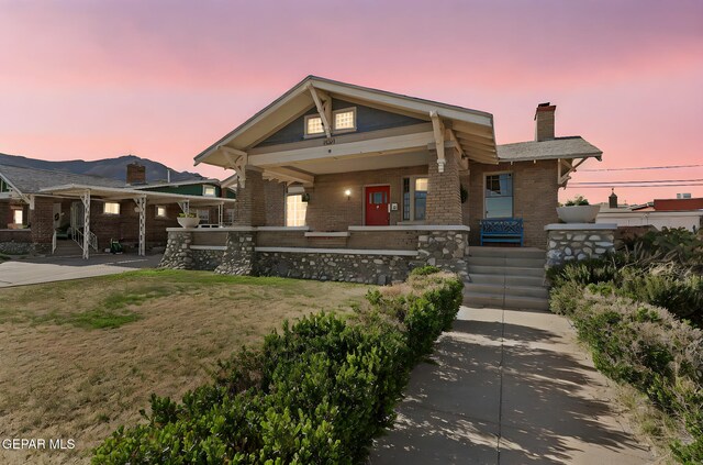 view of front of house featuring a chimney, brick siding, covered porch, and a yard