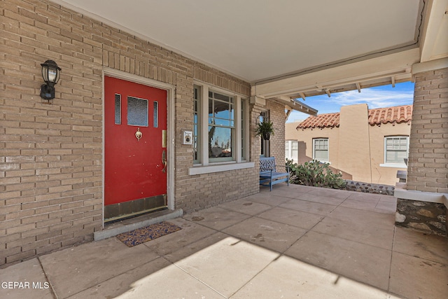 view of exterior entry featuring brick siding and covered porch