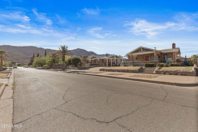 view of asphalt road with sidewalks, a mountain view, and curbs