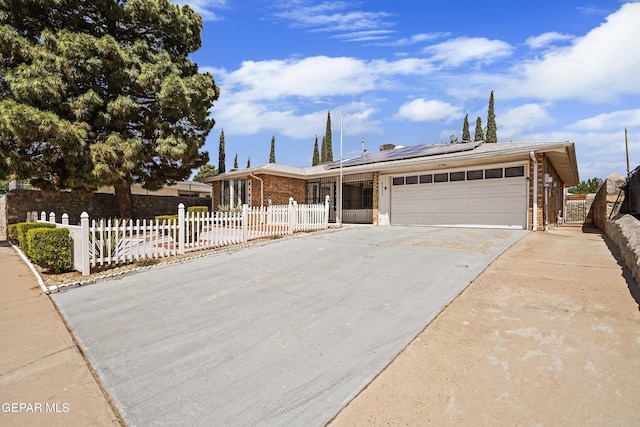 view of front of house with brick siding, an attached garage, roof mounted solar panels, concrete driveway, and a fenced front yard