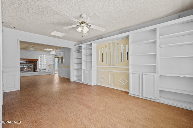 unfurnished living room with a ceiling fan, a textured ceiling, a brick fireplace, and wood finished floors