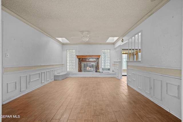 unfurnished living room featuring ornamental molding, a textured ceiling, a ceiling fan, a skylight, and wood finished floors