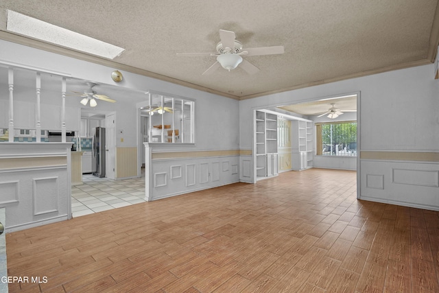 unfurnished living room featuring ceiling fan, a textured ceiling, light wood-style flooring, a wainscoted wall, and a decorative wall