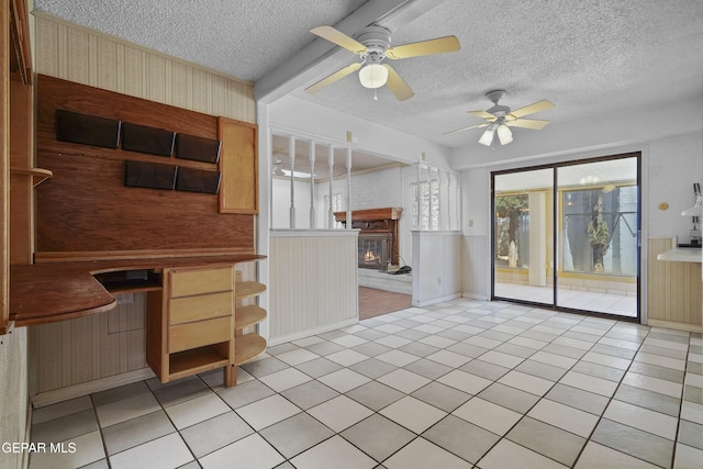 unfurnished living room with plenty of natural light, ceiling fan, a fireplace, a textured ceiling, and wallpapered walls