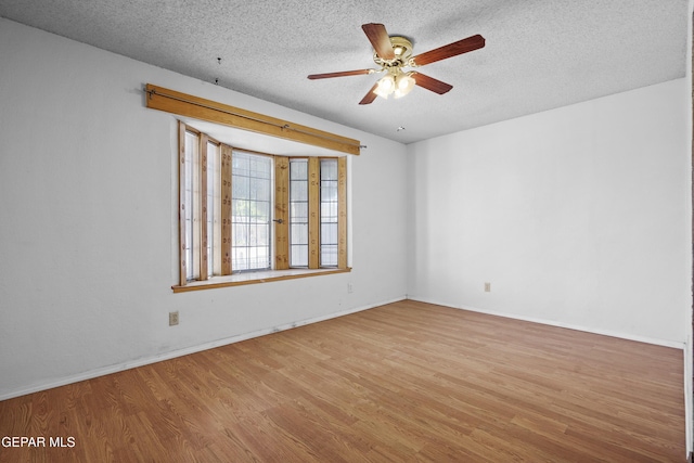 spare room with wood finished floors, a ceiling fan, a textured ceiling, and baseboards