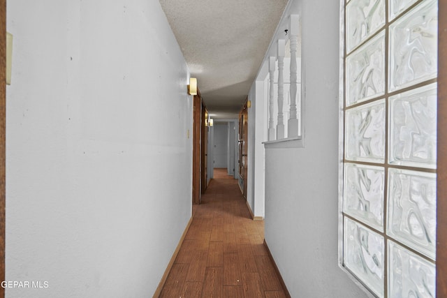 hall with wood finished floors, a textured ceiling, and baseboards