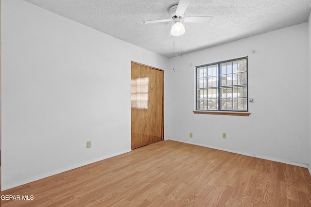 empty room with a textured ceiling, light wood-style flooring, a ceiling fan, and baseboards