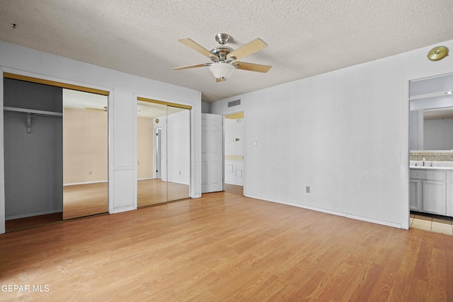unfurnished bedroom featuring two closets, light wood-style floors, connected bathroom, a textured ceiling, and baseboards