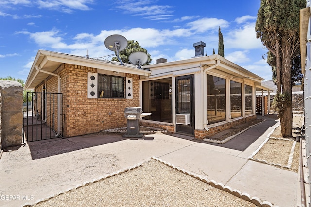 rear view of property featuring a sunroom, a gate, brick siding, and cooling unit