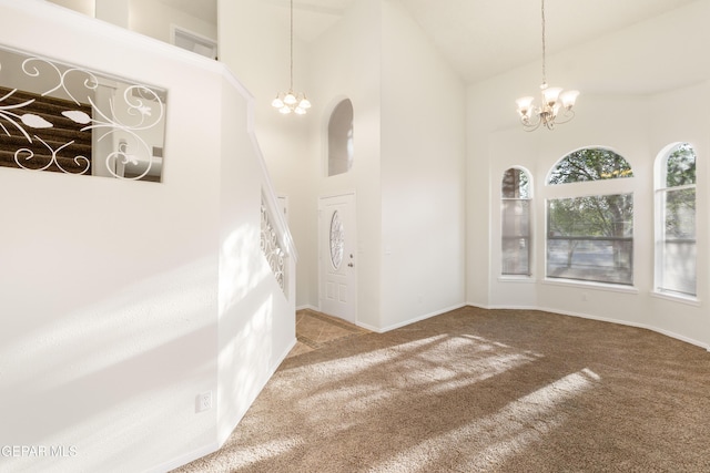 carpeted empty room featuring a chandelier, high vaulted ceiling, and baseboards