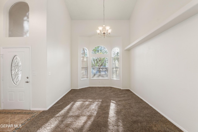 carpeted foyer entrance with a chandelier, baseboards, and a towering ceiling