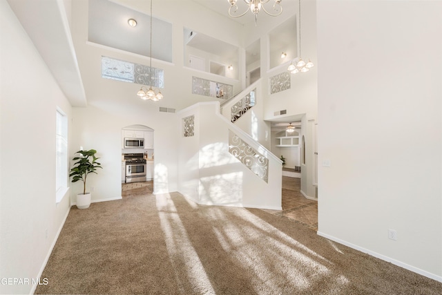 unfurnished living room with a chandelier, a high ceiling, arched walkways, and carpet