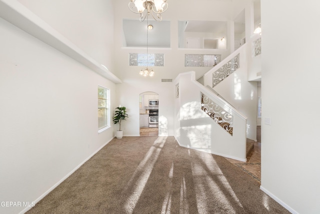 carpeted entryway with a chandelier, arched walkways, a towering ceiling, stairs, and baseboards