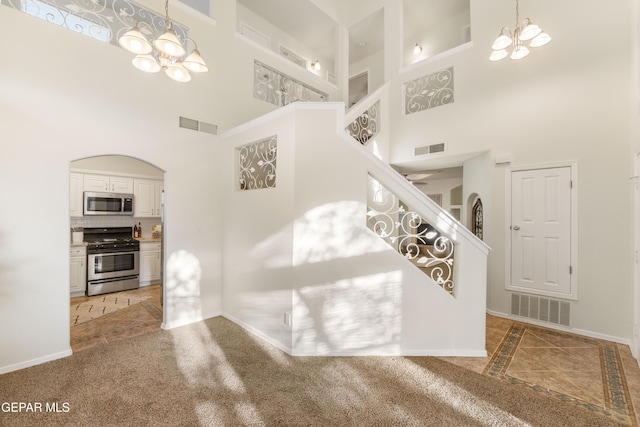 stairway featuring a towering ceiling, a chandelier, baseboards, arched walkways, and carpet flooring
