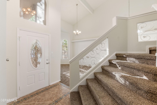 foyer entrance featuring stairway, inlaid floor details, high vaulted ceiling, a chandelier, and baseboards