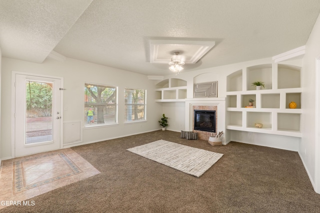 unfurnished living room featuring a textured ceiling, built in shelves, a tiled fireplace, carpet flooring, and baseboards