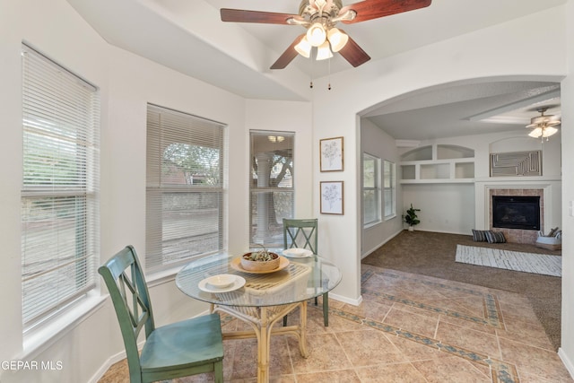 dining room with a ceiling fan, built in shelves, a tiled fireplace, tile patterned flooring, and arched walkways