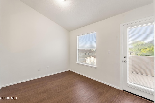 spare room featuring vaulted ceiling, dark wood-style flooring, and baseboards