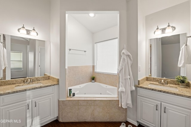 bathroom featuring wood finished floors, a tub with jets, and two vanities