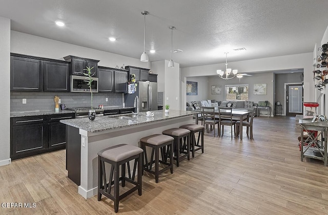 14840 Pebble Hills Blvd, El Paso, TX 79938 - kitchen featuring stainless steel appliances, a sink, dark cabinetry, a kitchen island with sink, and a breakfast bar area