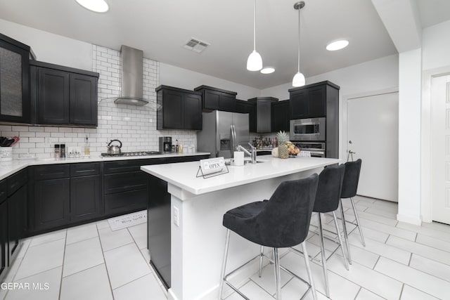 13673 Samlesbury Ave, Horizon City, TX 79928 - kitchen featuring stainless steel appliances, wall chimney range hood, a kitchen breakfast bar, dark cabinets, and light countertops