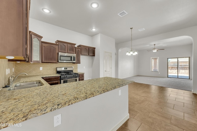 kitchen with stainless steel appliances, a sink, light stone countertops, arched walkways, and light colored carpet