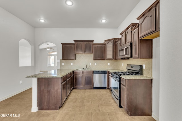 kitchen featuring stainless steel appliances, a peninsula, backsplash, light stone counters, and a sink