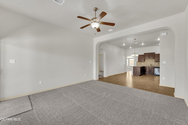 unfurnished living room with arched walkways, carpet, baseboards, and ceiling fan