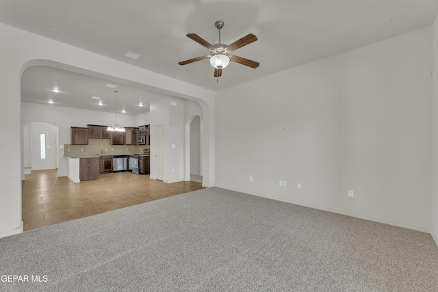 unfurnished living room with arched walkways, light carpet, a ceiling fan, baseboards, and a chandelier