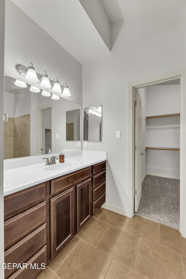 full bath with a walk in closet, vanity, and baseboards