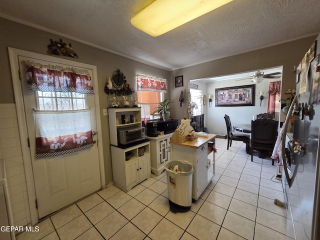 kitchen featuring light tile patterned floors, a textured ceiling, white cabinetry, a ceiling fan, and ornamental molding
