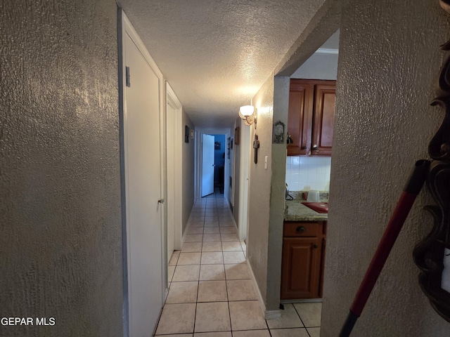 corridor with light tile patterned floors, a textured ceiling, and a textured wall