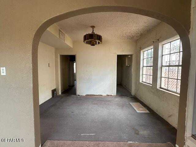 empty room featuring arched walkways, a textured ceiling, and a textured wall