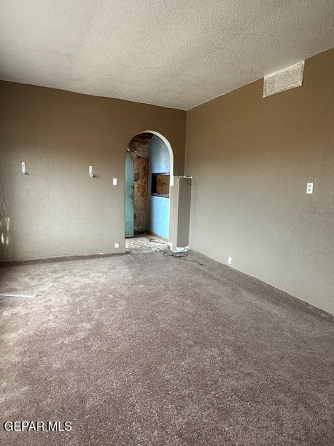 unfurnished room with arched walkways, carpet, and a textured ceiling