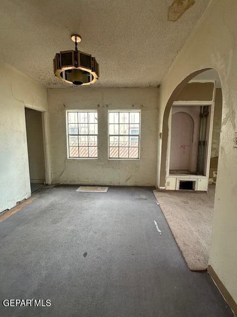carpeted spare room with a textured ceiling and arched walkways