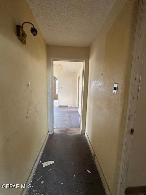 hall featuring a textured ceiling and baseboards