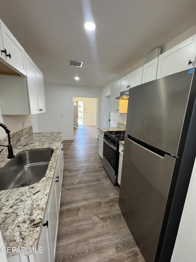 3512 Kemp Ave, El Paso, TX 79904 - kitchen with freestanding refrigerator, gas range, under cabinet range hood, dark wood-type flooring, and white cabinetry