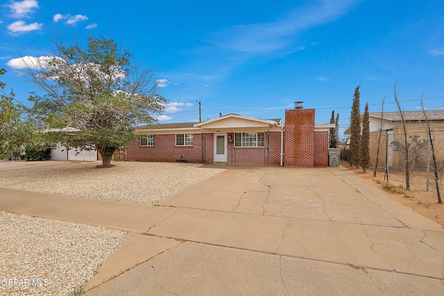 ranch-style house featuring driveway, fence, a chimney, and brick siding