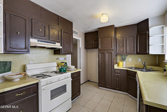 kitchen featuring white gas range, under cabinet range hood, dark brown cabinets, a sink, and light tile patterned floors