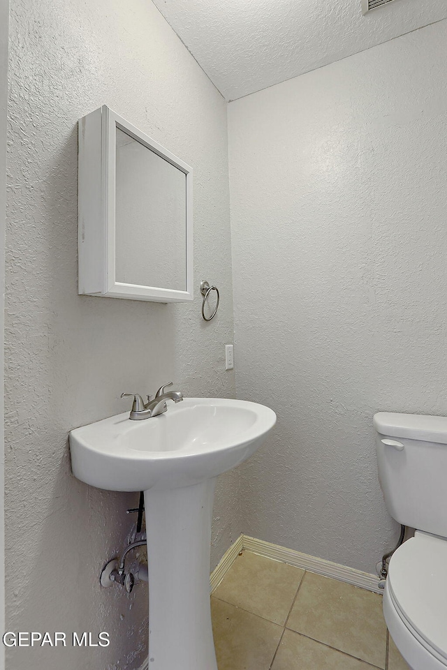 bathroom with tile patterned flooring, toilet, a textured ceiling, baseboards, and a sink