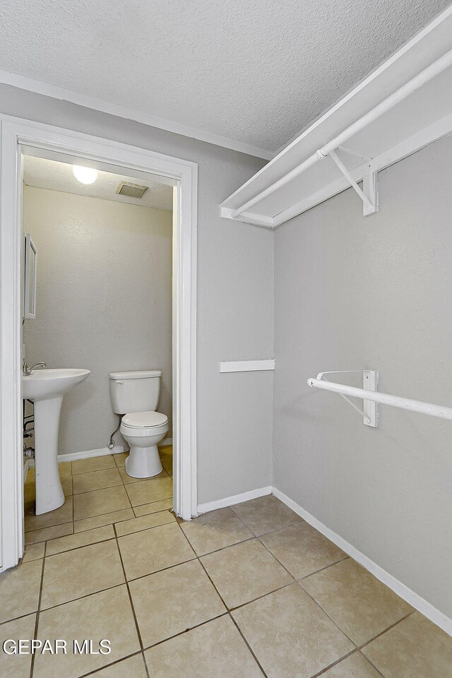 half bathroom with toilet, a textured ceiling, tile patterned flooring, a sink, and baseboards