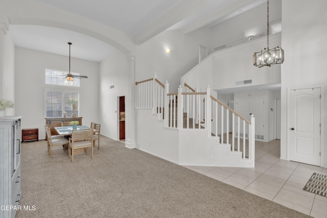carpeted dining space featuring a high ceiling, stairs, arched walkways, a ceiling fan, and tile patterned flooring