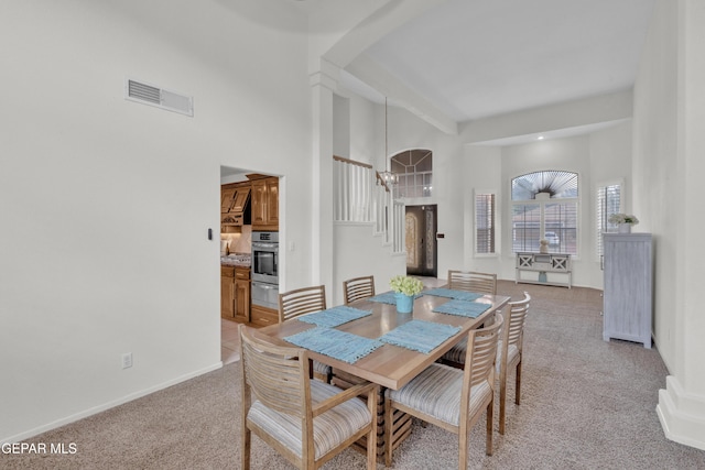 dining room with light colored carpet, a high ceiling, arched walkways, and baseboards
