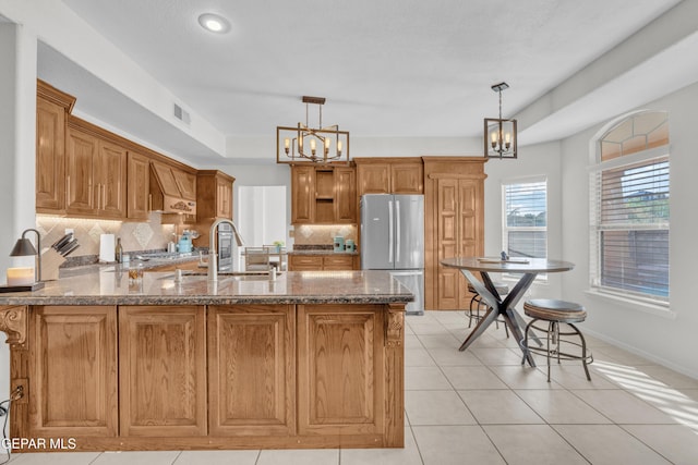 kitchen featuring freestanding refrigerator, a chandelier, a sink, a peninsula, and custom exhaust hood
