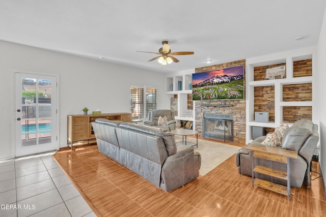 living room featuring a ceiling fan, plenty of natural light, a stone fireplace, and built in shelves