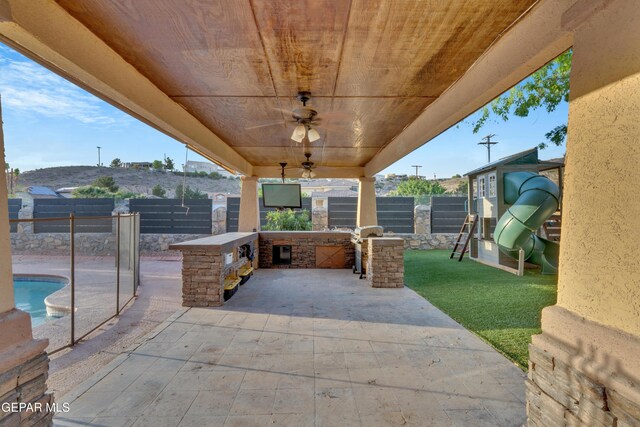 view of patio / terrace with a fenced backyard, exterior kitchen, ceiling fan, and a playground