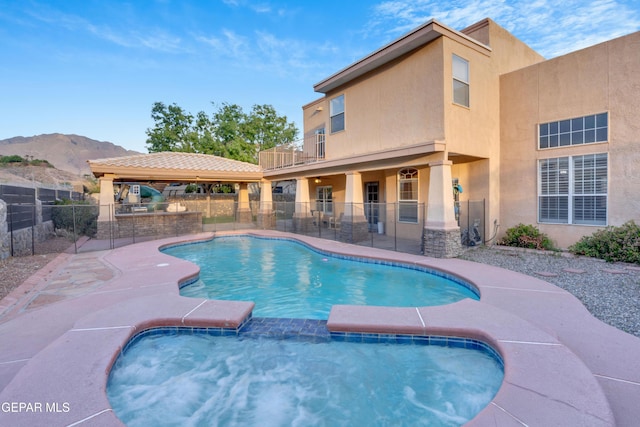 view of swimming pool with an outdoor kitchen, fence, a patio, a mountain view, and a pool with connected hot tub